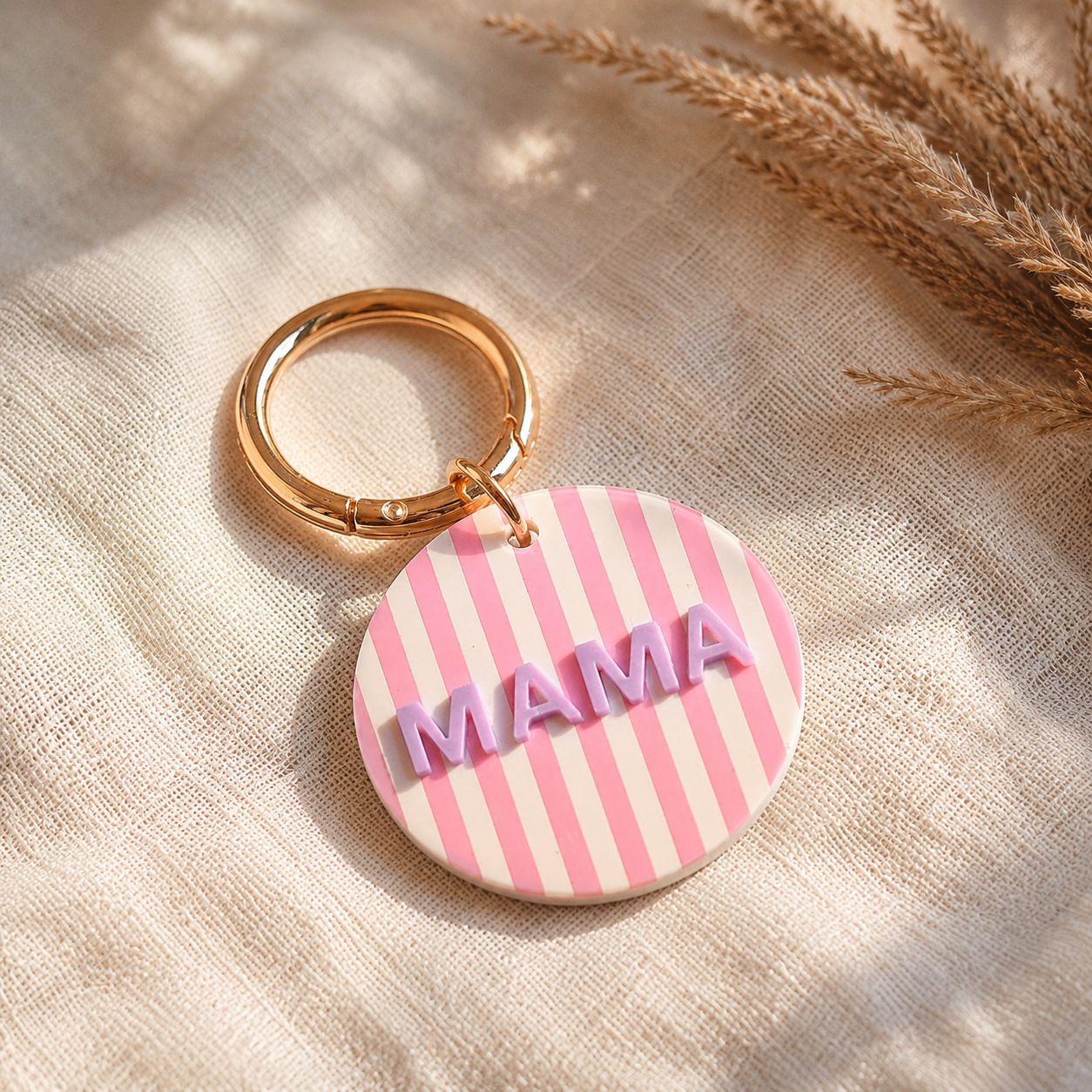 runder schlüsselanhänger in rosa-weiß mit goldfarbenem Ring und dem Schriftzug MAMA in flieder.
