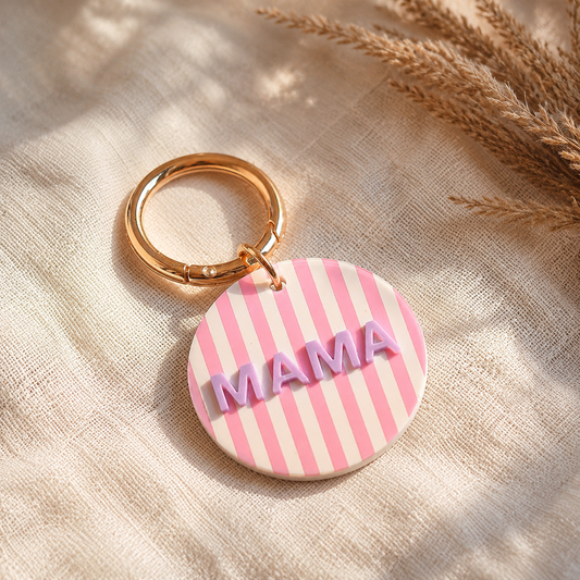 runder schlüsselanhänger in rosa-weiß mit goldfarbenem Ring und dem Schriftzug MAMA in flieder.