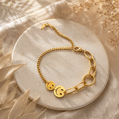 Goldenes Smiley-Armband aus Edelstahl auf hellem Boho-Hintergrund.