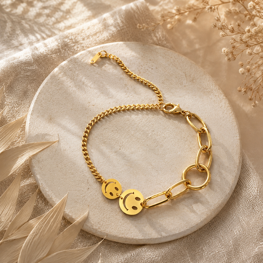 Goldenes Smiley-Armband aus Edelstahl auf hellem Boho-Hintergrund.
