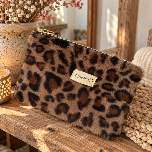 Flauschiges Leo-Täschchen aus weichem Fellimitat in Braun und Schwarz mit goldfarbenem Reißverschluss und süßem HAPPY-Label mit Smileys, dekoriert auf einem Holztisch im Boho-Stil.